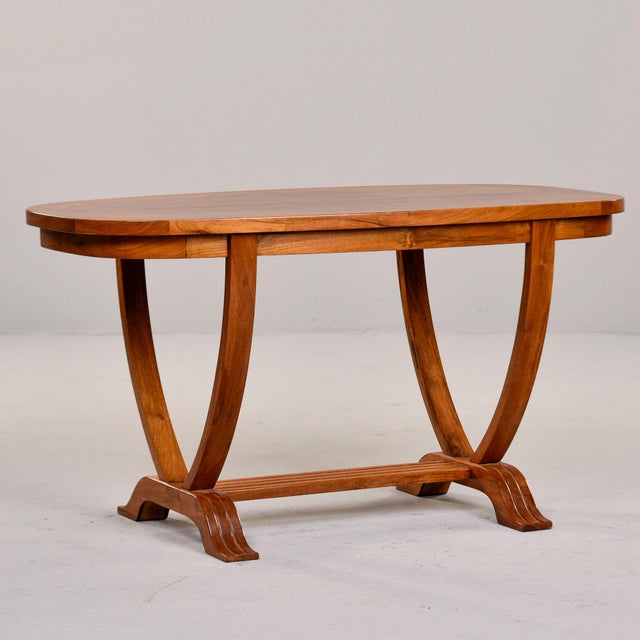 This French Art Deco coffee table presents an oval top in blonde hardwood, supported by two curved leg pairs that taper...