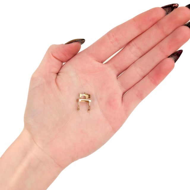 A fine vintage gold charm. In 14 karat yellow gold. In the form of a sewing machine atop a table. With an integral bail...