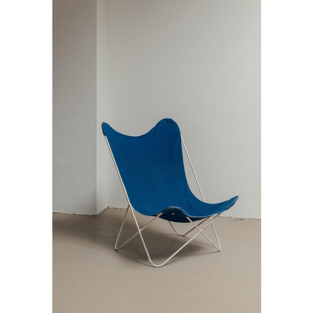 1970’s patinated butterfly chair with hocker. Famous white lacquered steel frame with a seat in thick blue and black...
