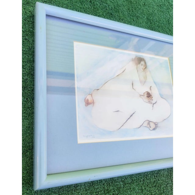 A small framed signed print by RC Gorman of Woman with child. The print has been framed in a pale blue frame with blue matte.