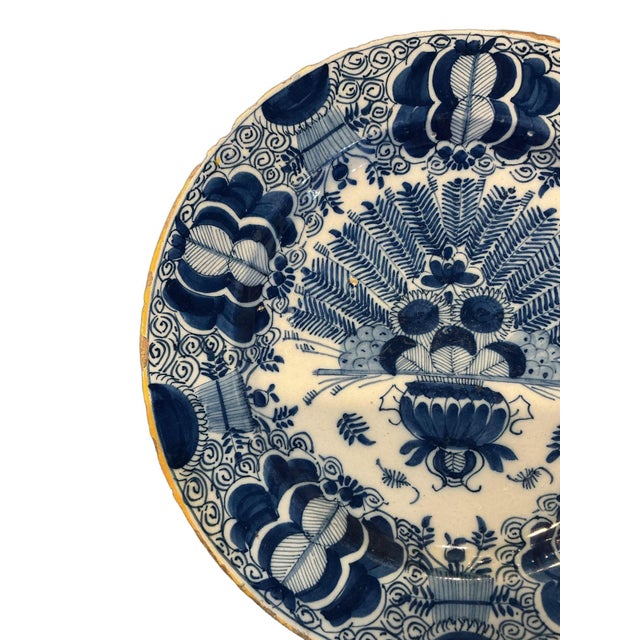 This is a classic piece of Delft. The central motif shows a decorative urn overflowing with flowers and large palm/fern...