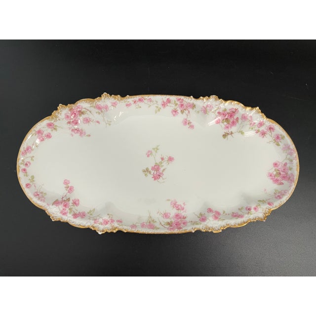 An antique Charles Field Haviland celery dish, featuring delicate clusters of pink roses against an embossed, scalloped...