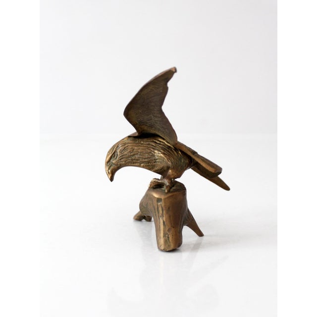 A vintage brass eagle sculpture in a dynamic landing pose, perched atop a branch and tree stump base. Rich feather...