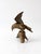 A vintage brass eagle sculpture in a dynamic landing pose, perched atop a branch and tree stump base. Rich feather...