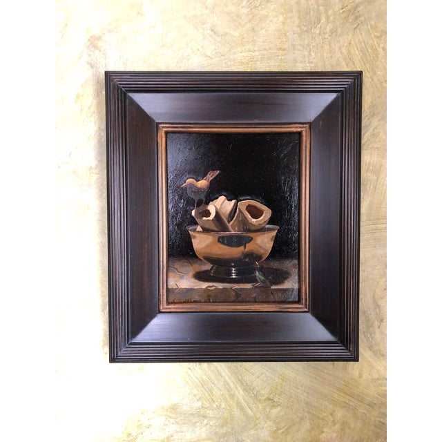 This oil on panel artwork features a striking still life of a shiny bowl filled with bone fragments, contrasted against a...