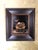This oil on panel artwork features a striking still life of a shiny bowl filled with bone fragments, contrasted against a...