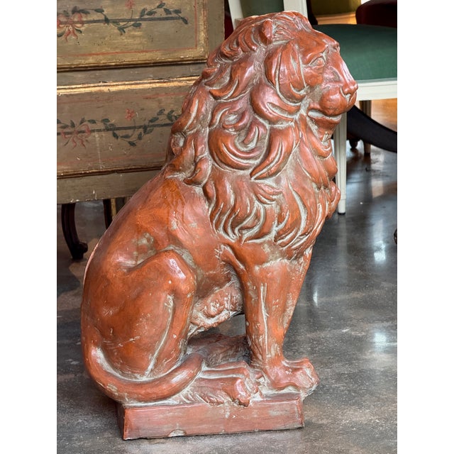 Terra cotta figure of a lion seated upright on a rectangular plinth base, modeled with a full flowing mane worked in deep...