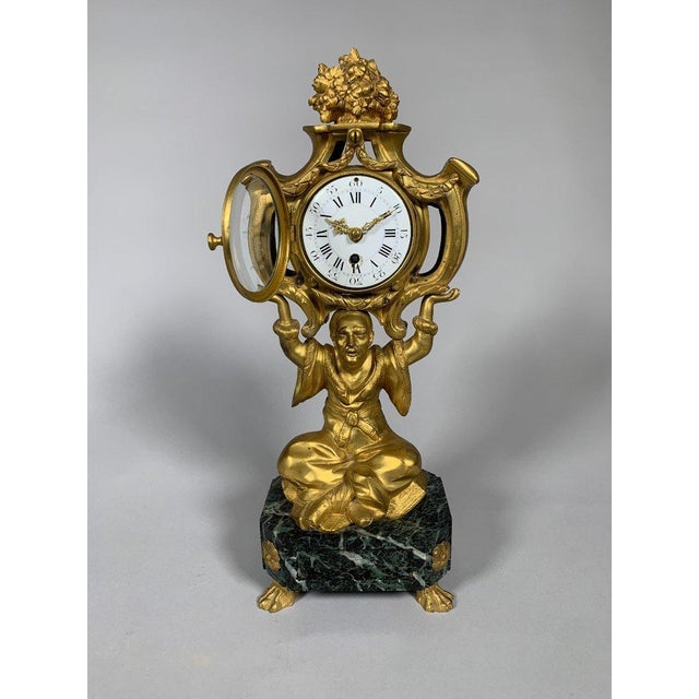 A Louis XV style Chinese clock, early 19th century. It depicts a Chinese figure seated cross-legged supporting a rocaille...