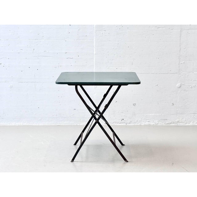 This folding table combines timeless design with practical functionality. The square metal tabletop in a subtle green...
