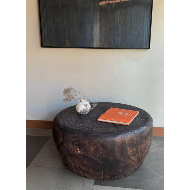 A striking sculptural coffee table carved from a substantial piece of solid suar wood, celebrating the raw beauty and...