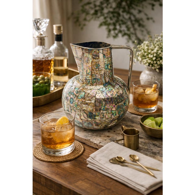 A striking 1960s Mexican modernist pitcher crafted in alpaca silver with intricate abalone shell mosaic inlay, executed in...