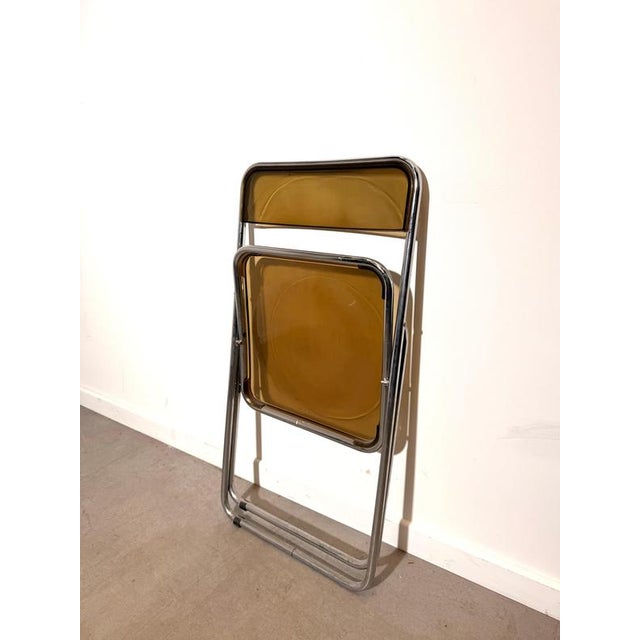 iconic folding chair in the manner of Giancarlo Piretti,. The chair features a smoked amber transparent polycarbonate seat...