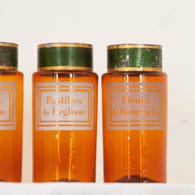 Dimensions: 9-⅜”H x 4-⅛”Diameter Six amber glass apothecary jars with their original green and gold tin covers from...