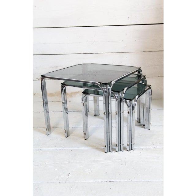 Set of three stackable nest tables in chromed metal and smoked glass, 1960s. This set of coffee tables is made unique by...