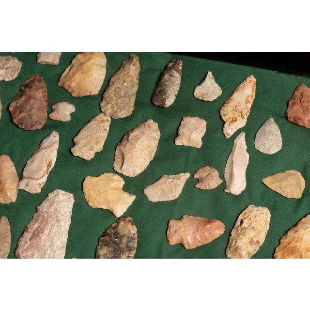 Collection of Native American stone arrowheads and projectile points presented in a black wood display frame against a...