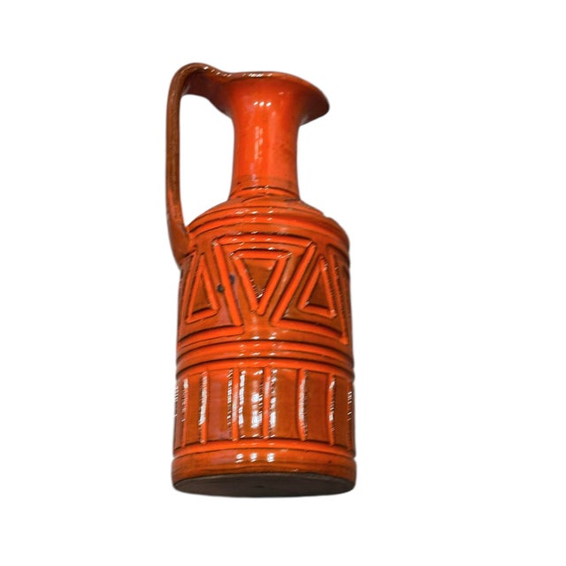 This hand-crafted ceramic jug features intricate geometric relief patterns and a vivid orange glaze, perfect as a...