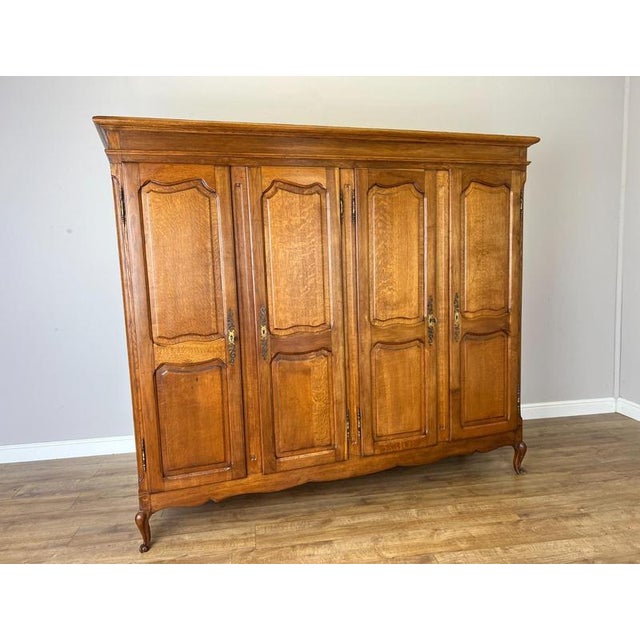 A handsome Vintage French Louis wardrobe in Oak, featuring four panelled doors, an elegant moulded cornice and gracefully...