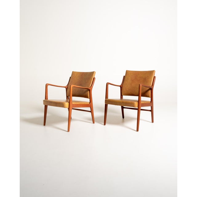 Set of two armchairs with a teak frame, contoured armrests, and tapered legs. Padded seat and backrest, upholstered in...
