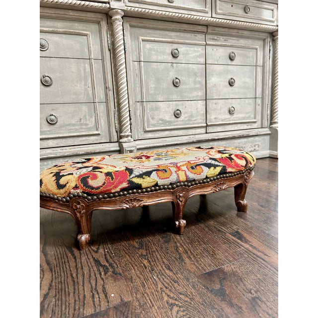 A charming vintage Louis XV-style footstool featuring a hand-worked needlepoint upholstered top with vibrant floral and...