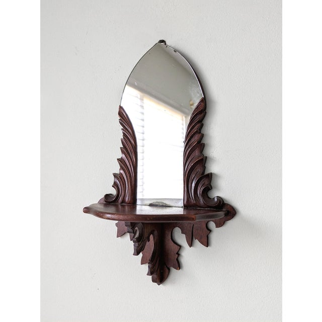 A pair of antique curio wall-hanging shelves featuring a flourishing carved leaf design and mirrored back plate.