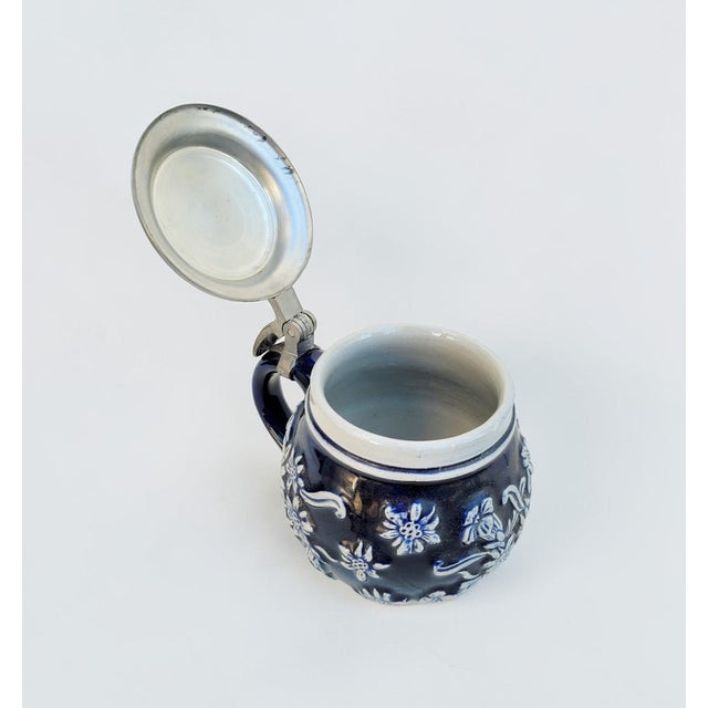 A highly decorative and beautifully preserved German stoneware stein from the 1940s–1950s, distinguished by its rich...