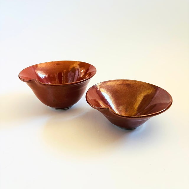 A set of 2 vintage studio pottery nesting bowls. Reddish glaze. Each is signed on the bottom. Overall measures 6.75"W x...