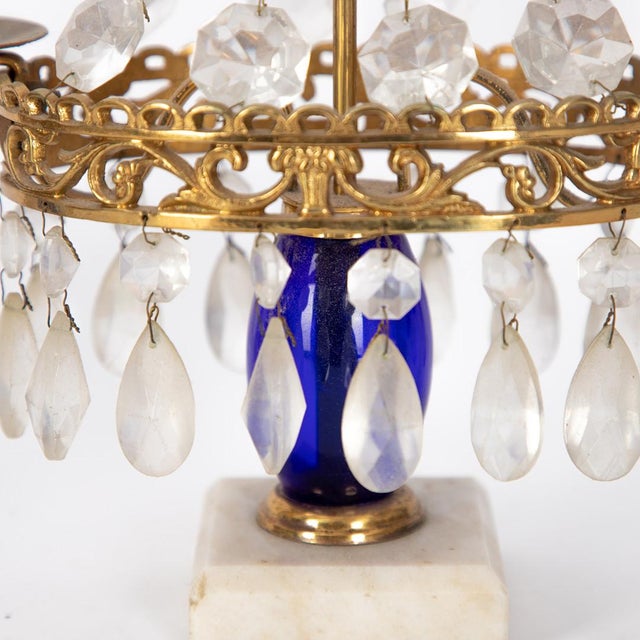 A charming pair of Swedish crystal prism candelabra featuring gilt brass mounts, white marble bases, and striking cobalt...