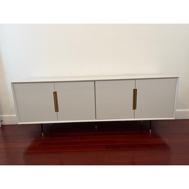 Elegant ivory painted linen sideboard featuring clean architectural lines and warm brass hardware accents. This piece...