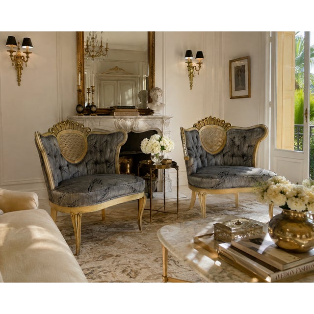 A beautiful pair of vintage Hollywood Regency lounge chairs featuring elegant carved wood frames, decorative cane back...