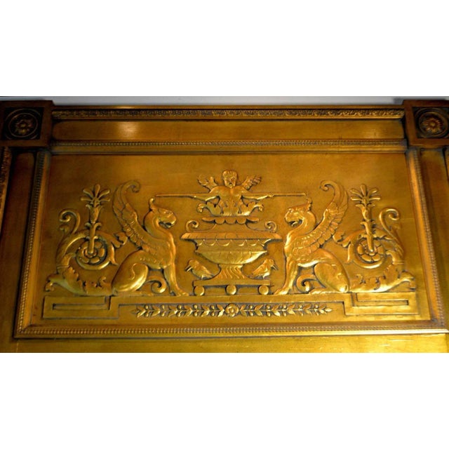 Empire-style giltwood looking glass, the frame with projecting floral block-carved corners surrounding a carved frieze...
