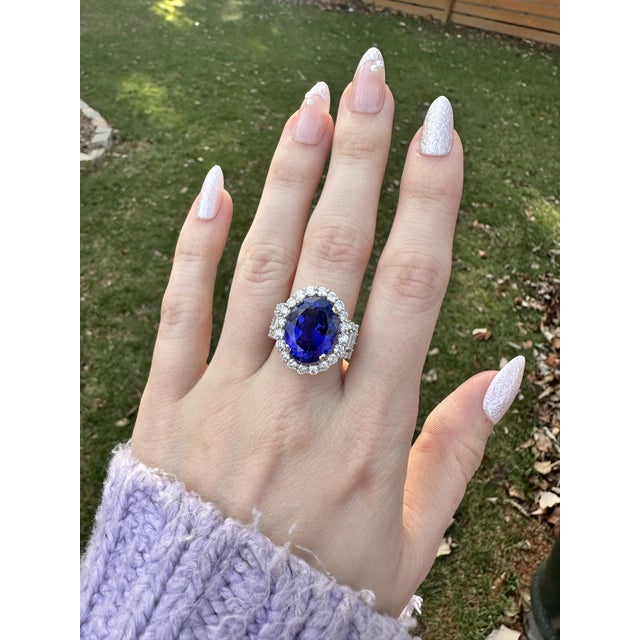 A tanzanite rests in a deep violet-blue at the centre of this solid 14K white gold ring, surrounded by fifty-eight earth-...