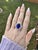 A tanzanite rests in a deep violet-blue at the centre of this solid 14K white gold ring, surrounded by fifty-eight earth-...