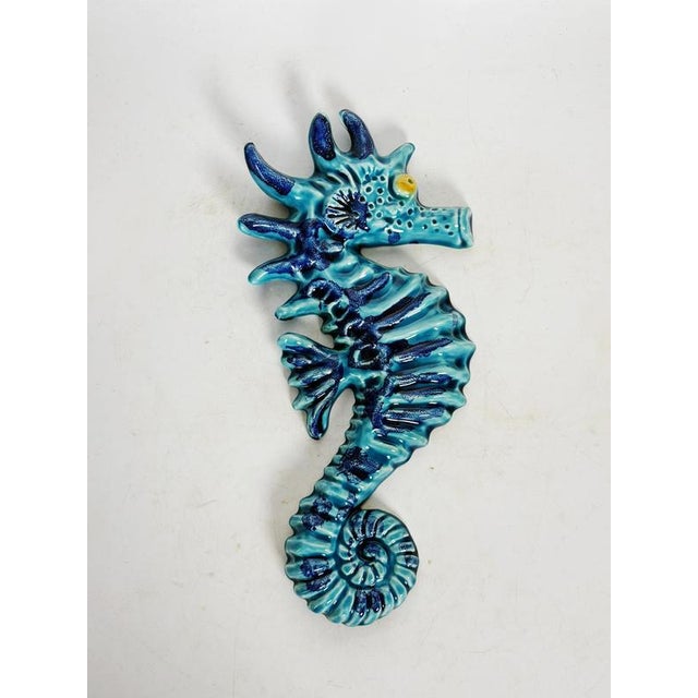 A blue glazed ceramic wall decoration, France, 1970s, depicting a stylized seahorse with expressive and textured forms....
