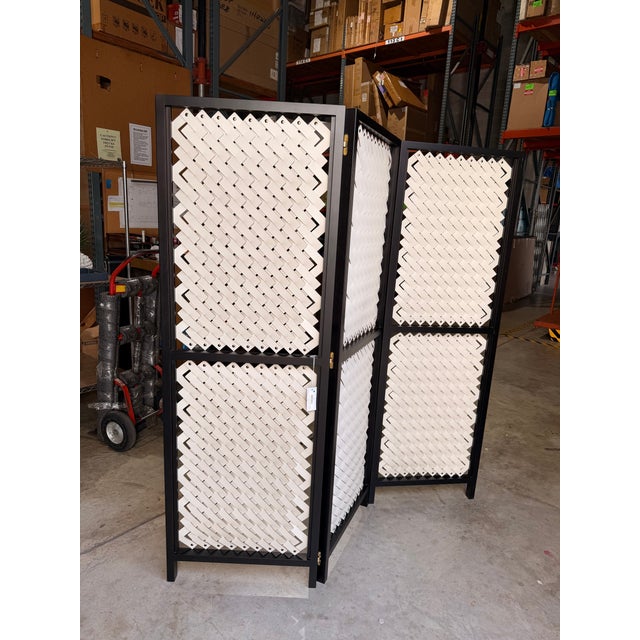 Contemporary room divider featuring a bold black wood frame with handwoven cream leather panels that create a striking...