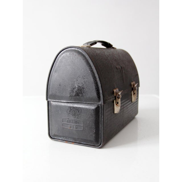 A vintage Thermos lunch box featuring an arched lid, embossed Thermos “T” logo, and a beautifully worn black finish. Its...