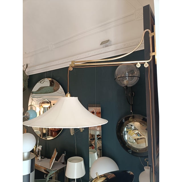 Wall-mounted lamp with a swivel arm and pulley system. The brass structure is hinged to the base, allowing the light to be...