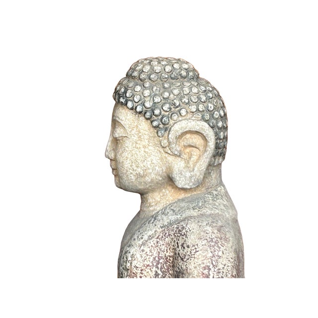 This weathered stone sculpture depicts a seated Buddha, carved with a serene expression and poised in a traditional...