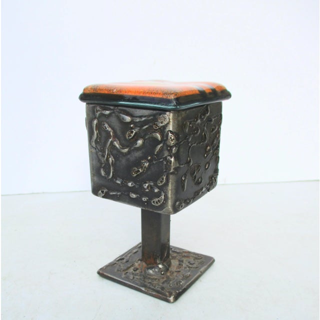 Art Brut footed container with art glass tile lid. Handmade steel walls and stemmed foot. Decorated with steel welding...