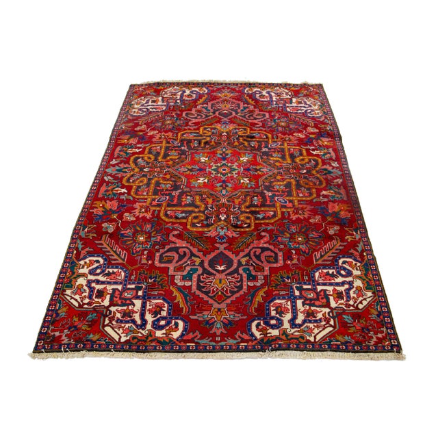 This vintage Heriz handmade wool rug has a red field with multicolor accents all over the design. This rug measures 6'2''...