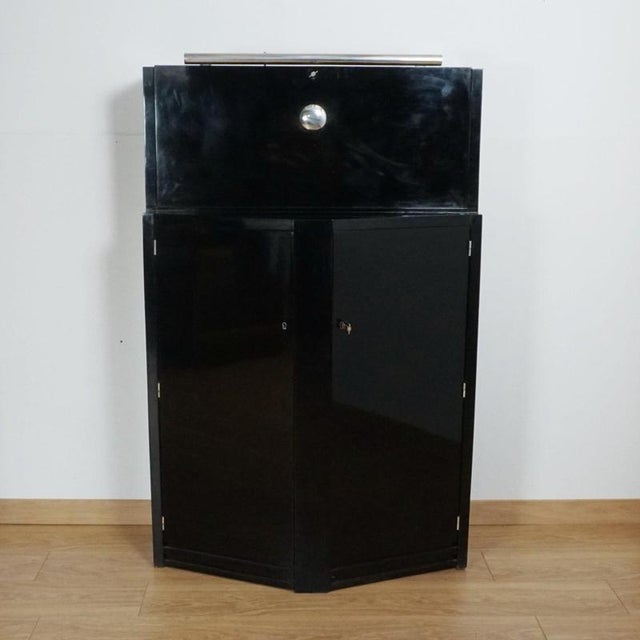 An Art Deco ebonised drinks cabinet. Upper chrome handled drop down mixing section with a lower oak lined bottle storage....