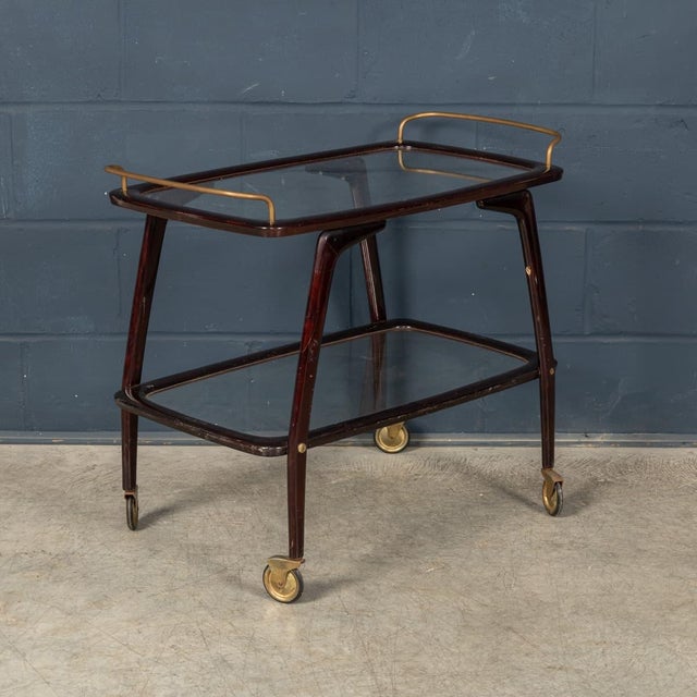 An elegant Italian drinks trolley dating from the 1960s, combining a sculptural dark-stained wood frame with refined brass...