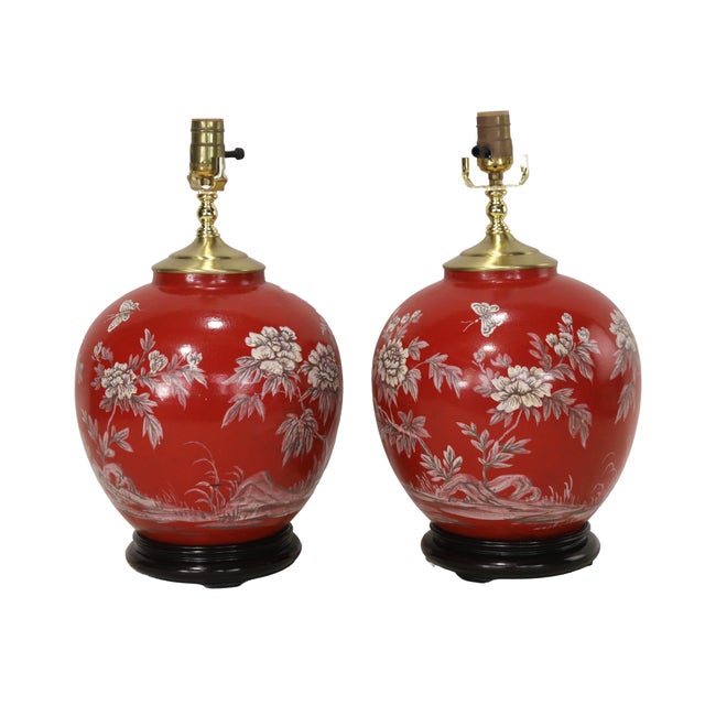 The lamps feature a classic ginger jar shape and are adorned with a vibrant, rich coral red. The ceramic bodies are hand-...