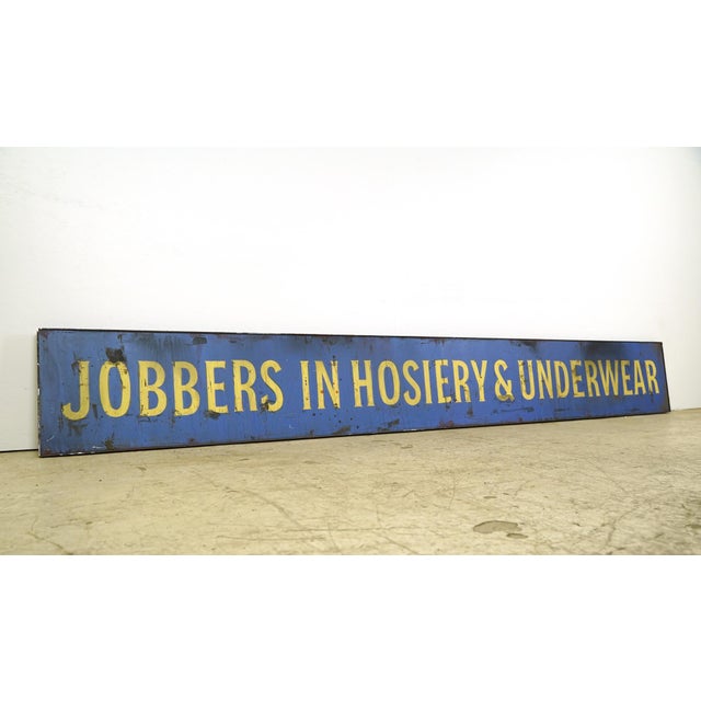 Reclaimed movie set sign made of aluminum in a blue and yellow color. The sign reads "Jobbers in Hosiery & Underwear"....