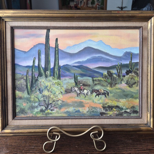 This vintage framed landscape painting by artist Jo Solomon depicts a desert scene centered around saguero cacti. The...