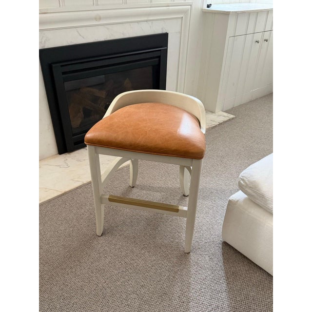 Set of three custom-made counter stools in toffee leather with antique white wood frame and brass footrest rail by Jessica...