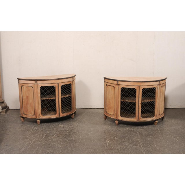 A French pair of wooden demi console cabinets, with wire panel front doors, from the mid 20th century. These mid-century...
