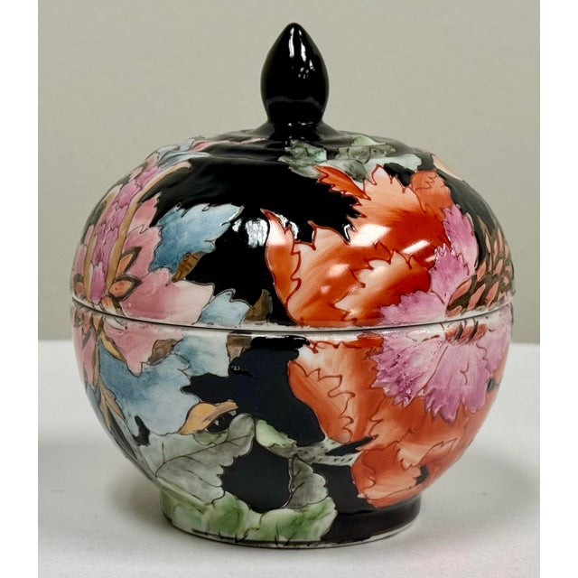 Petite vintage Asian chinoiserie lidded ceramic ginger jar adorned with a black enamel base and pinks, rust, gold and...
