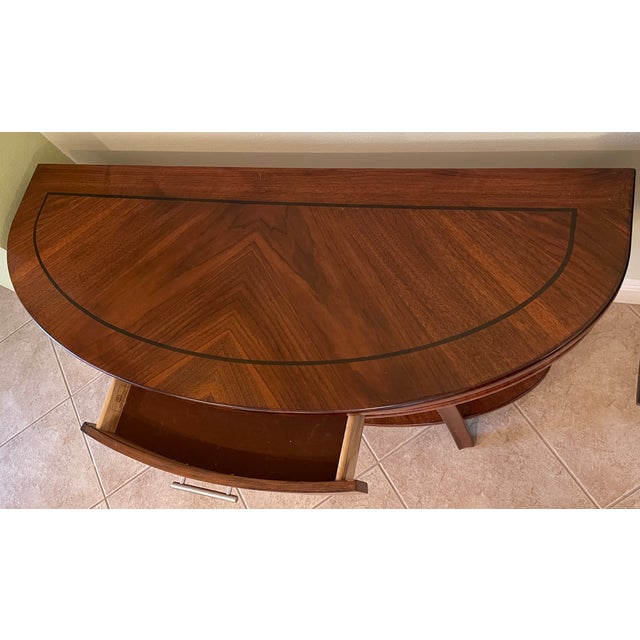 Polished wood console table has a demilune shape with a chevron veneer pattern on the top surface. The piece includes a...