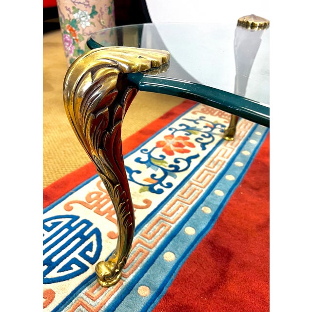 Elegant mid century bronze and glass coffee table with thick glass beveled top held aloft by four chased gilt bronze palm...