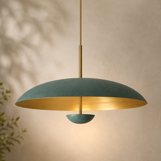sculptural pendant light featuring a broad, gently curved dome shade in a rich green finish with a warm brass-toned...